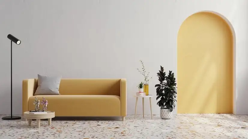 تصویر اتاق نشیمن با دیوار سفید و مبل راحتی زرد با چراغ و گیاه